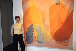 Megan Wolfkill, a Memphis native who just moved to Cincinnati for her residency at Manifest, stands beside her painting Orange Couplet, which features bright tones and slightly asymmetrical mirror images.